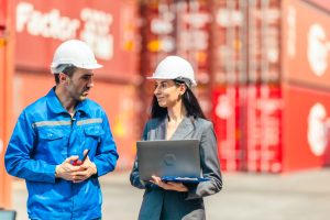 Industrial container workers discussing eco-friendly logistics strategies. Reducing fuel consumption, lowering carbon footprints, and implementing zero-emission practices in supply chain operations.